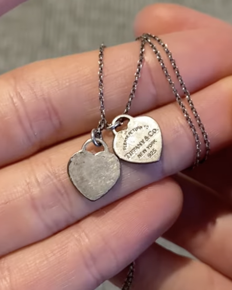 Tarnished silver necklace with Tiffany & Co heart charms held in hand, before cleaning at home